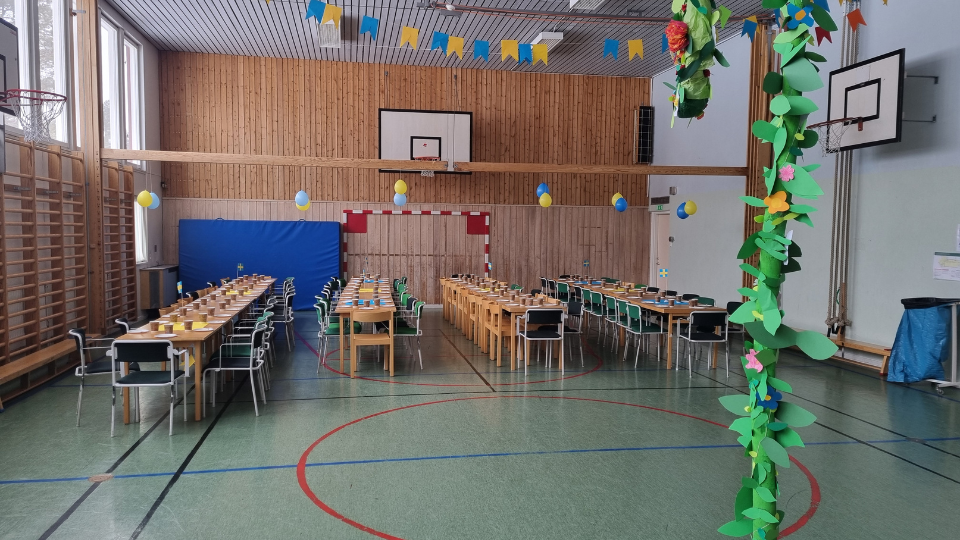 Gympasalen i Hakkas är utsmyckad till ett midsommarfirande med en midsommarstång i förgrunden