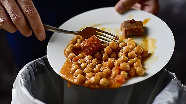 Bilden illustrerar hur någon häller ut mat i sopkorgen
